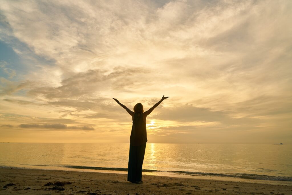 positive person with arms spead wide standing on beach at sunset