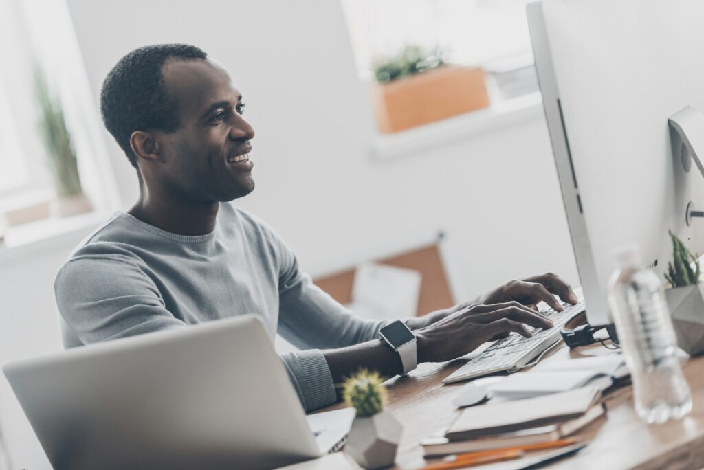 smiling man working on computer at a desk using tool that puts your social media on autopilot