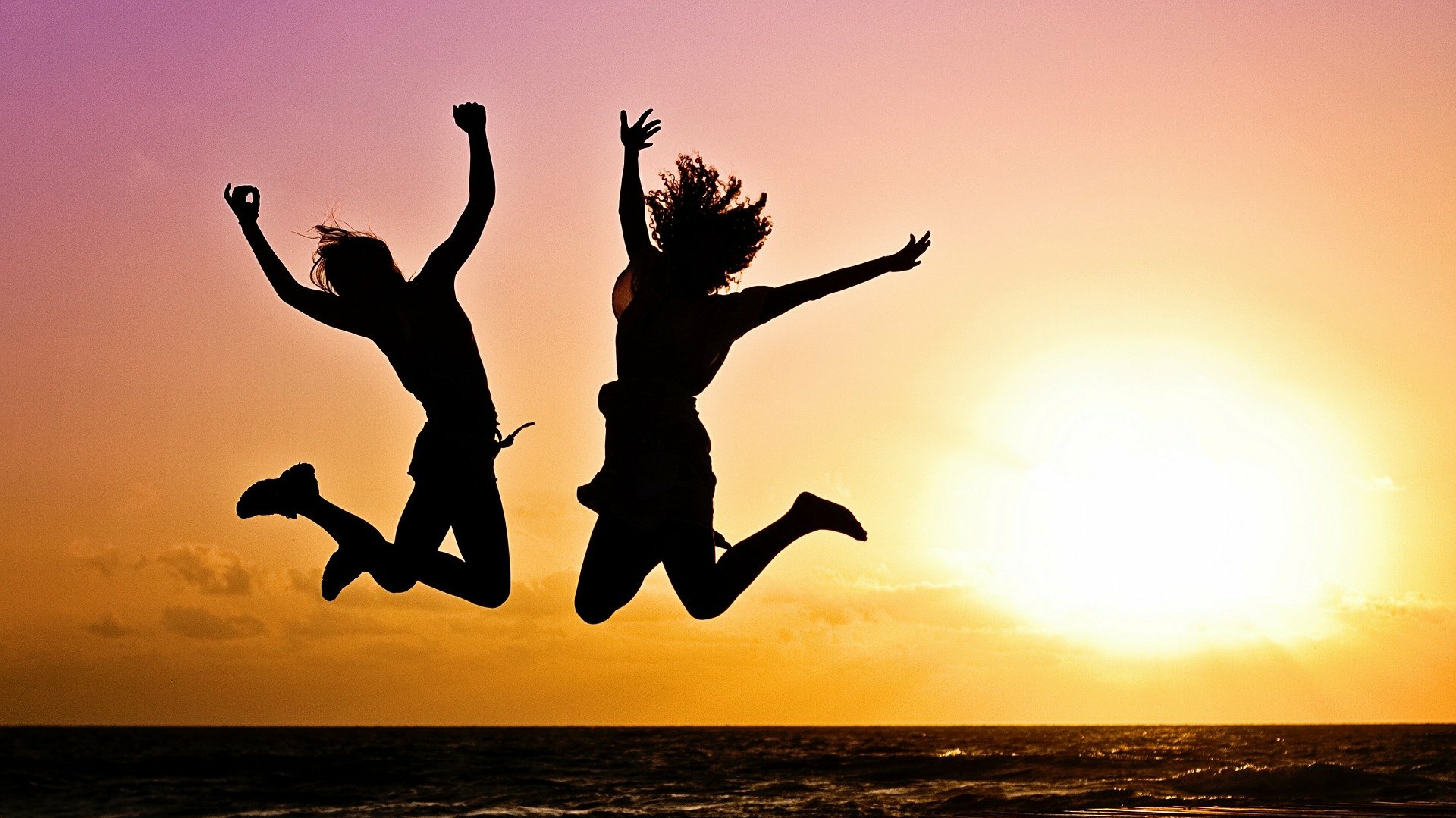 two people excitedly jumping up on a beach at sunset
