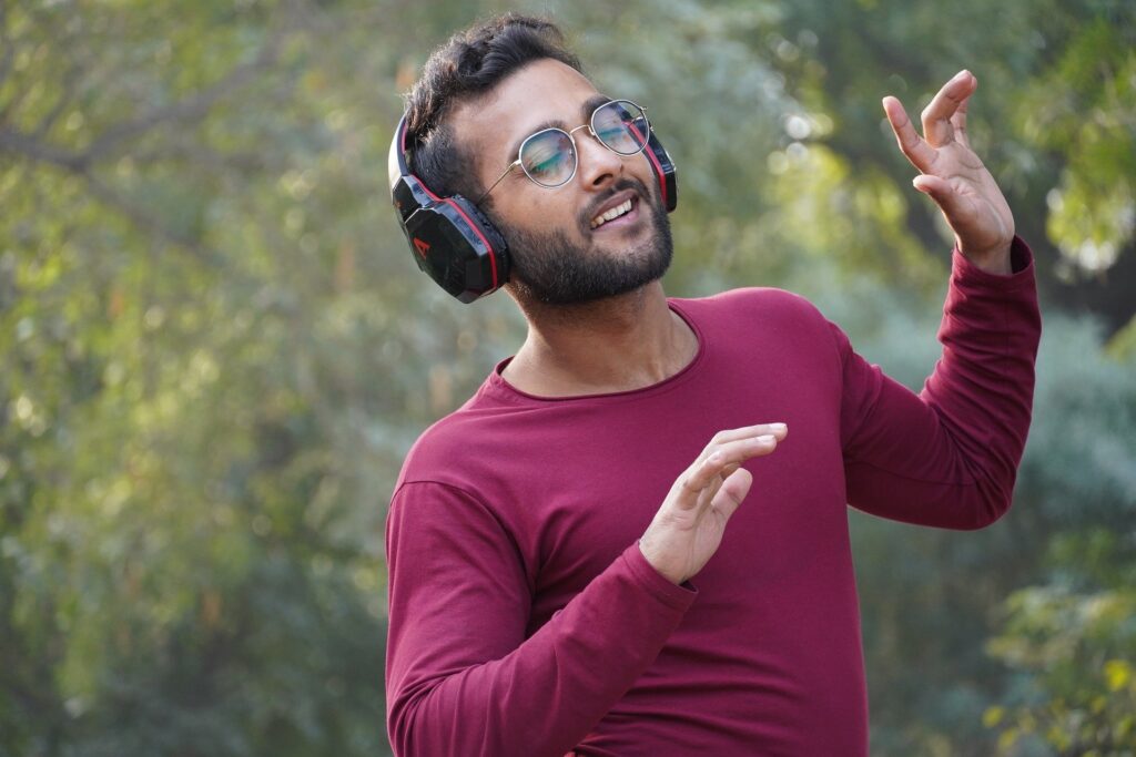 man wearing glasses in purple jumper with headphones on listening to podcasts outdoors