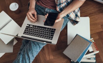 person writing a blog on a laptop with phone in hand