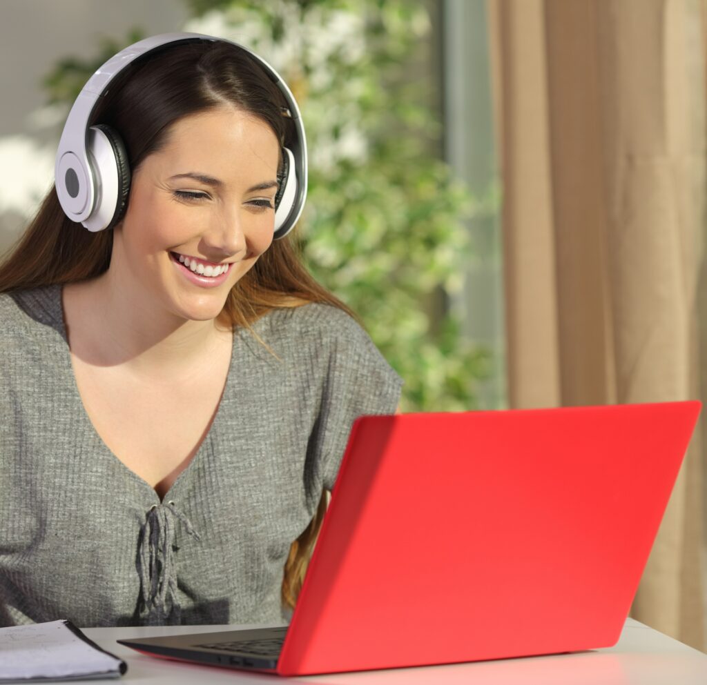 smiling woman wearing headphones recording a podcast on a red laptop