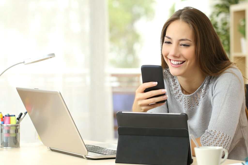 smiling woman sitting at desk reading 9 crucial must have pages on your websites blog post on her smartphone