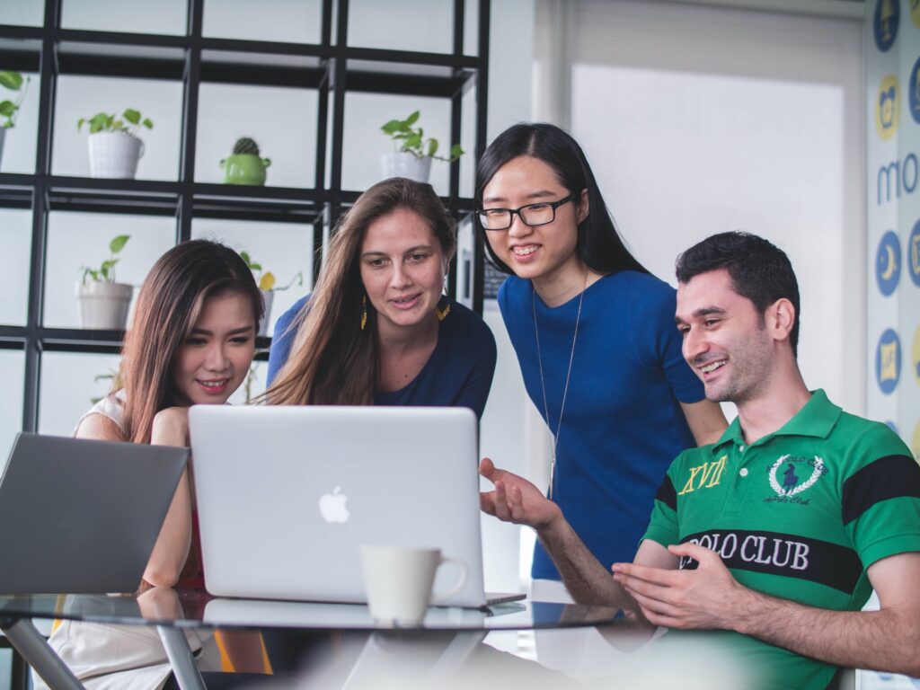 4 friends crowded round a laptop engaged by a website they are looking at