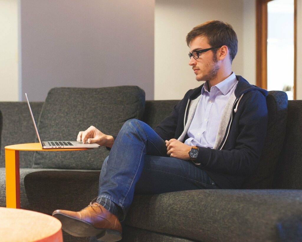 man wearing glasses sitting on sofa working on laptop writing persuasive sales copy