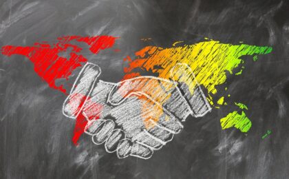 shaking hands drawn in chalk in front of a world map on a blackboard