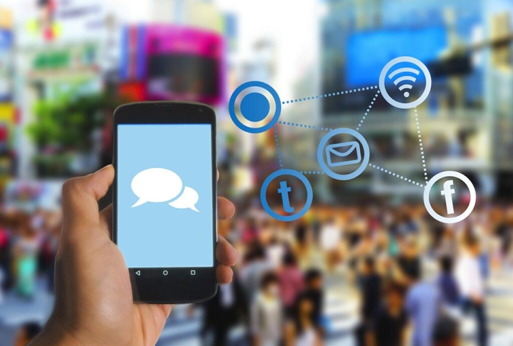 hand holding smartphone with speech bubbles on scree and floating social media icons