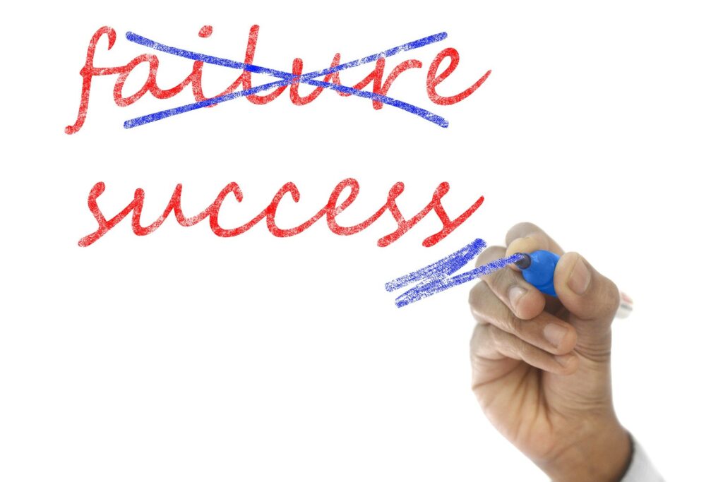 the words failure and success written in red pen on a whiteboard with a hand holding blue pen crossing out the word failure