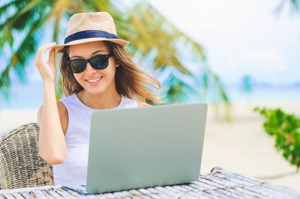 female market leader wearing sunhat and sunglasses sitting outside at table with laptop writing guest blog