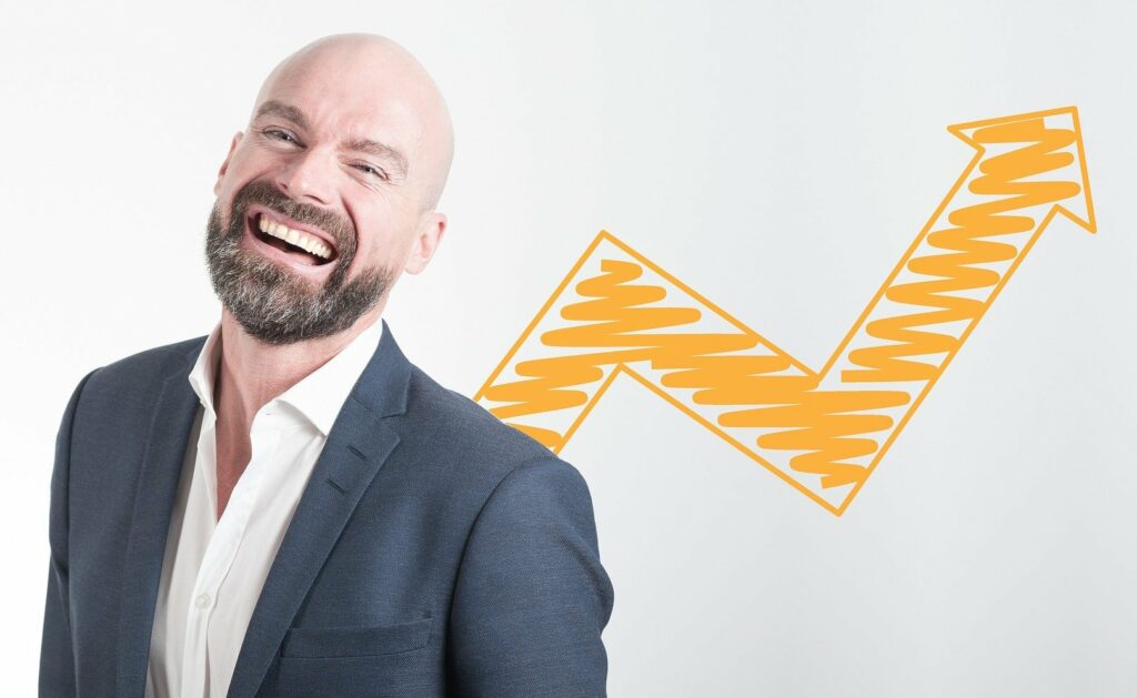 smiling bearded man in a suit with increased profits arrow on board behind him after applying 5 simple tweaks to increase your profits