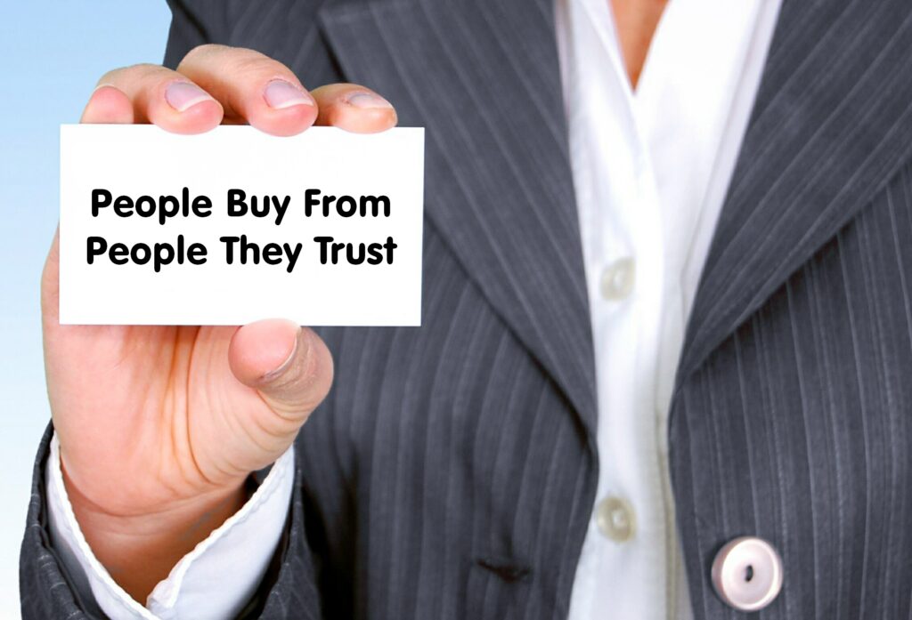 customer in a suit holding a card that says people buy from people they trust