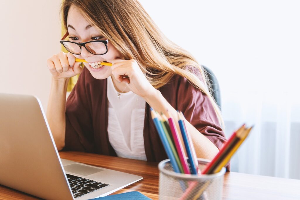 woman wearing glasses with a pencil in her mouth sitting at laptop reading 6 tips for selling to businesses blog